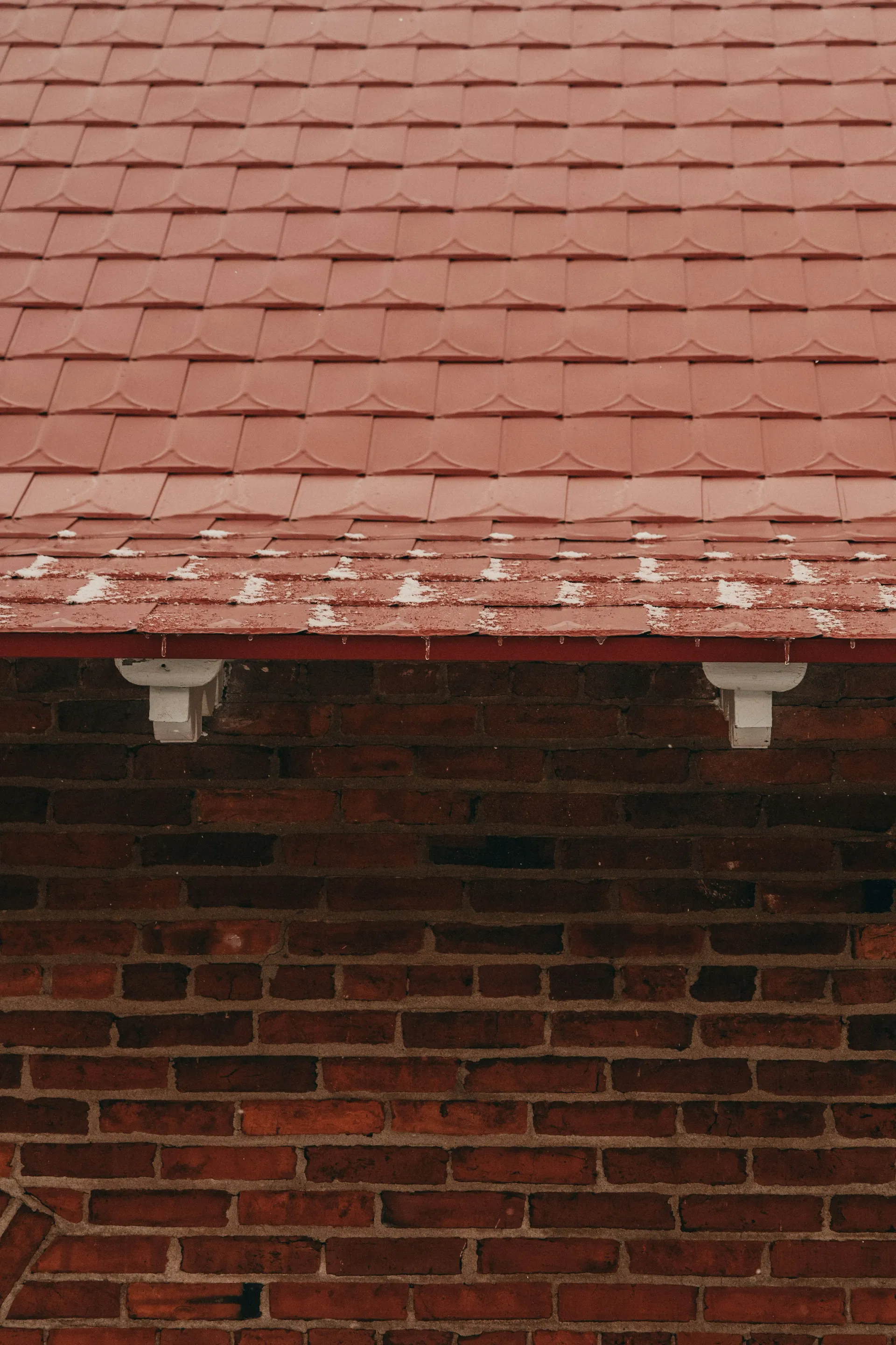 A close-up image of a well-maintained red tiled pitched roof with a brick wall beneath, illustrating quality concrete tile roofing and the effects of winter weather, common on homes in Spalding, Peterborough, and across Lincolnshire.